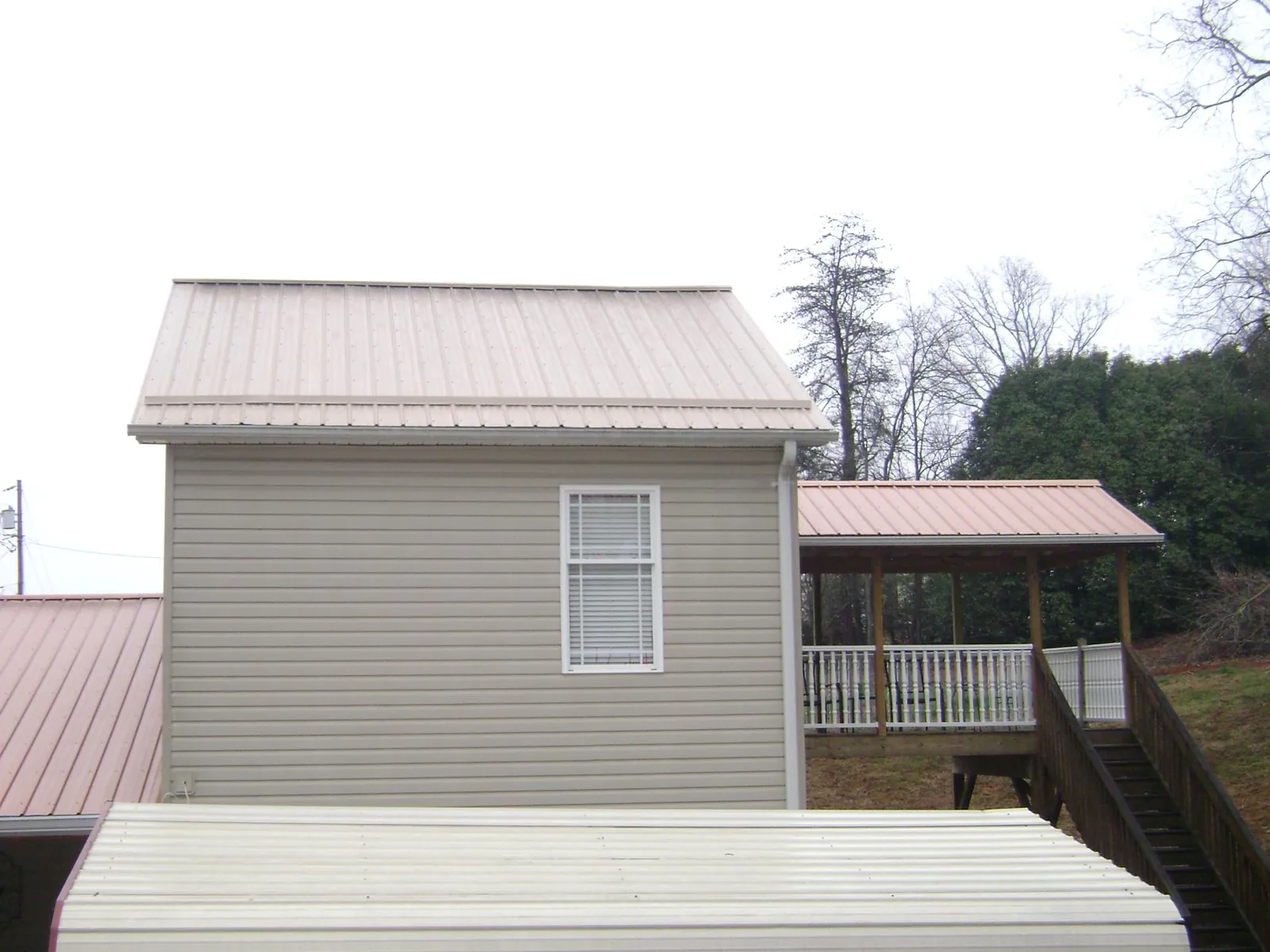 Tan metal roofs on a two story addition and attached porch, from a Roof Replacement job in Wilton